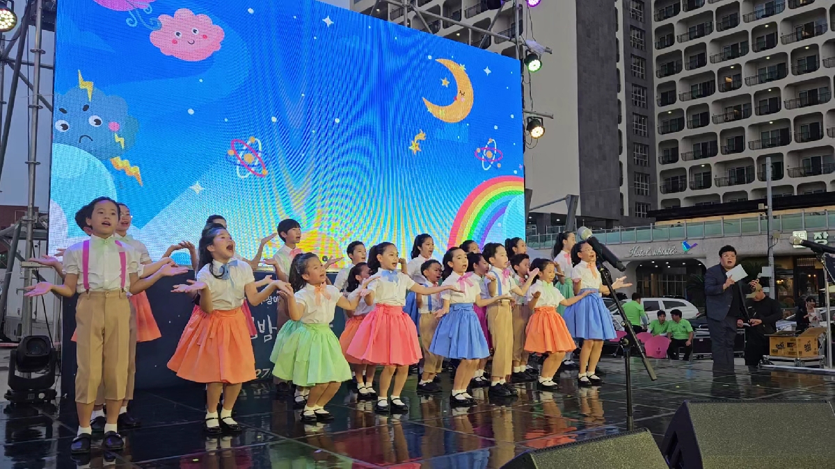 어린이 합창단 자자의 합창 모습, 형형색색의 옷을 입고 율동을 하고 있다.